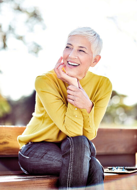 Porträt einer lächelnden Frau mit grauen, kurzen Haaren im Freien