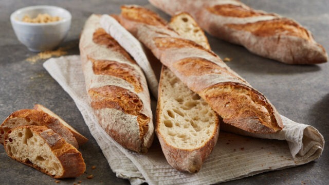 Drei gebackene Baguettes mit GMI_Slow Milling mit goldbrauner Kruste, eins ist aufgeschnitten