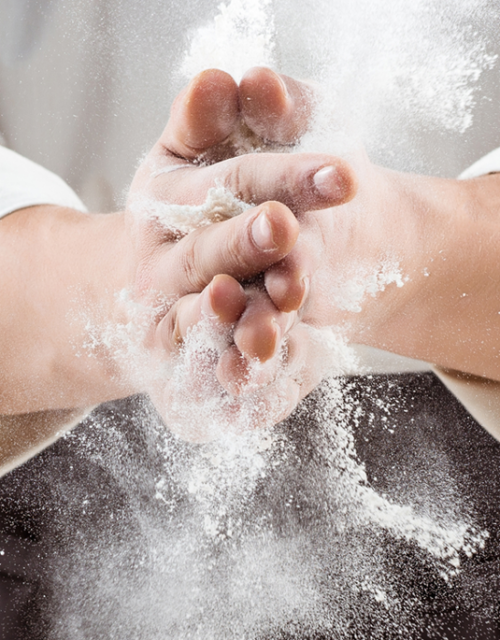 Die Hände eines Bäckers schlagen zusammen, sodass sich das Mehl verteilt