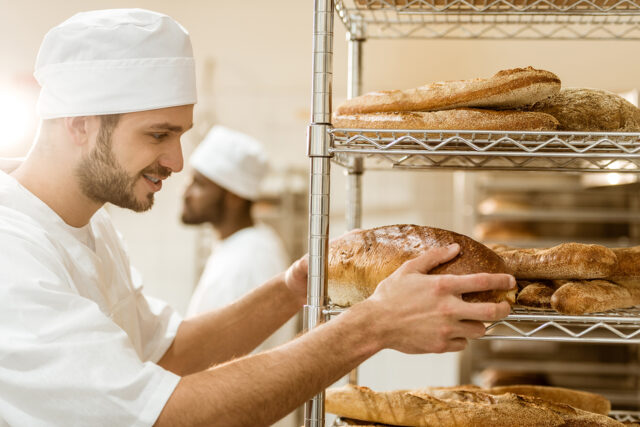 lächelnder Bäcker, der frisches Brot in einer Backstube in Regale einräumt