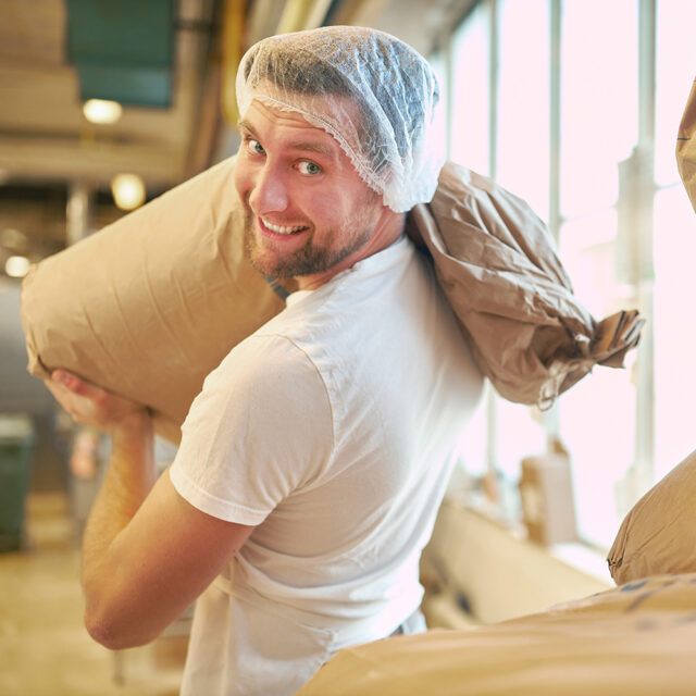 Bäcker oder Müller trägt einen großen Sack Mehl.