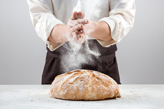 Die Hände eines Bäckers schlagen über einem rustikalen Bio-Brot zusammen