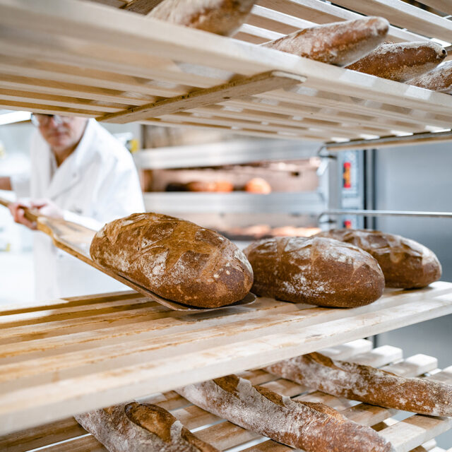 Brote mit Mehl bestäubt werden in einer Bäckerei mit Holzschieber auf Holzregale gelegt.