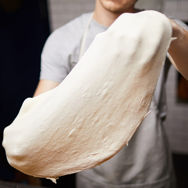 Junger Bäcker, der einen Pizzateig in den Händen hält